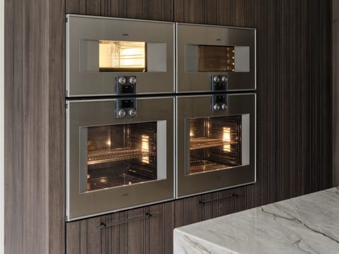 A Gaggenau 400-Series oven wall — four ovens set into dark Leicht Bahia timber cabinetry, with the Platino quartzite worktop in the foreground — in the Keston kitchen project.