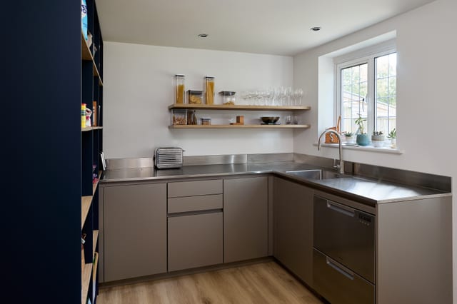 The tall Leicht cabinetry wall at Hever: full-height runs in Fenix Boreal Green carry the AEG appliance stack, an open display niche and a deeper drinks niche, reading as one continuous elevation.