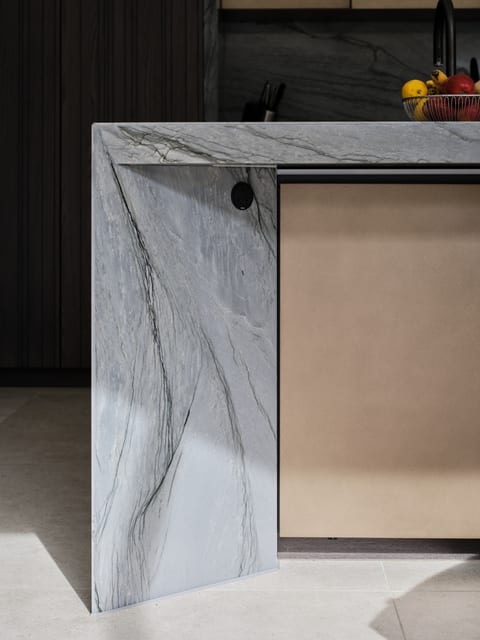 Close detail of the Keston island showing the Platino quartzite carried down into a wide stone leg, with the bronze island back and dark timber cabinetry behind.