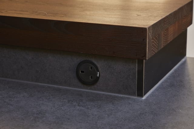 Detail of the thick Danish timber top at Eltham meeting the dark Dekton surface, with a recessed power socket.