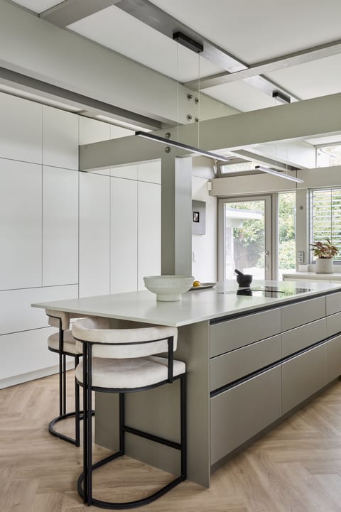 The bronze metallic island in the Oxted kitchen, with a Caesarstone top and dining chairs, white cabinetry behind and a HUF HAUS beam overhead.