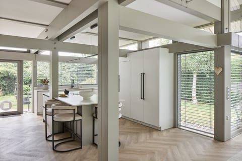 The HUF HAUS timber columns and beams running through the Oxted kitchen, with the bronze island and dining stools set within the structure.