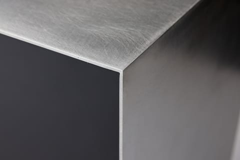 Macro detail of the handmade stainless steel island's welded corner, the brushed steel meeting the matt black Fenix body.