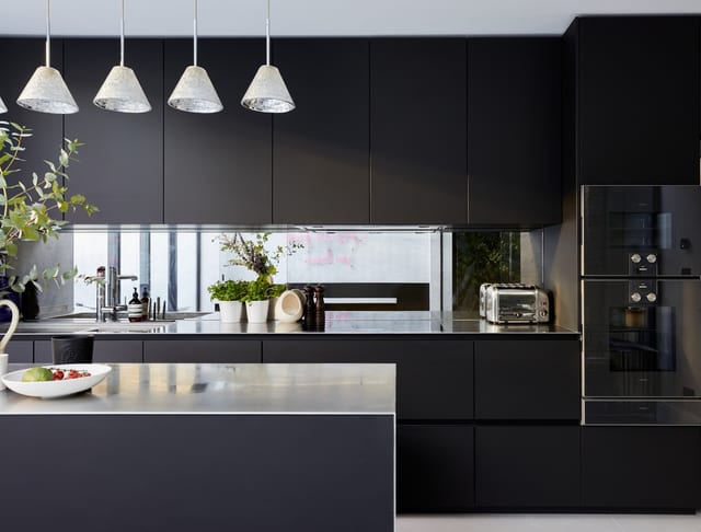 The matt black Fenix Leicht run at Hammersmith, carried to the ceiling with a shadow-gap detail, stainless worktop and antique-mirror splashback, with the stainless island in the foreground.