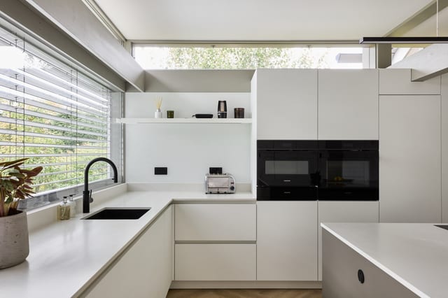 A corner of the main Oxted kitchen — white cabinetry and a Caesarstone worktop with a black tap and integrated Siemens ovens, below a clerestory window.