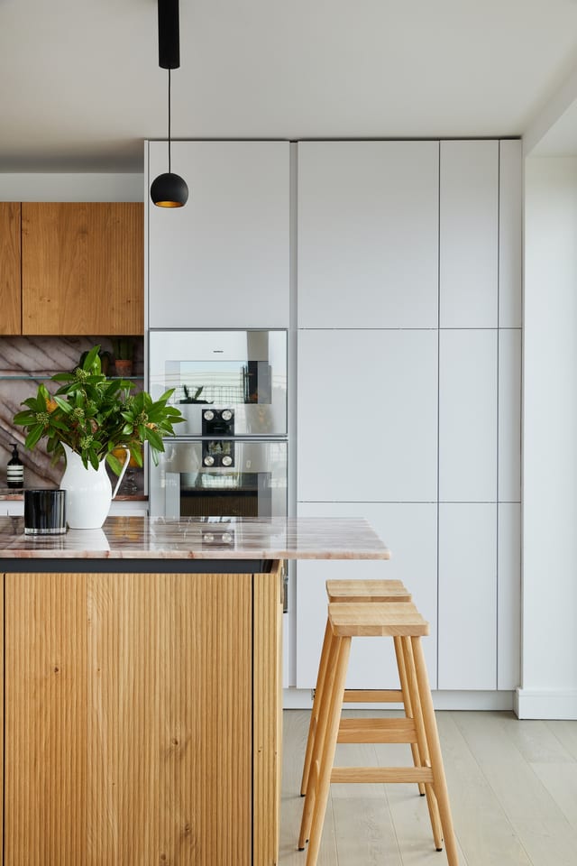 Soft white Leicht tall cabinetry carrying the integrated Gaggenau appliances, beside the routed-oak island and Cosmopolitan Quartzite worktop.
