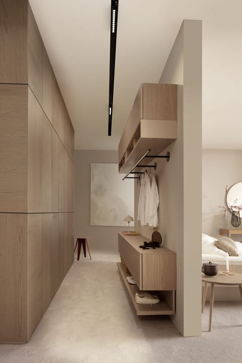 A Sudbrock dressing-room scene: a tall light-timber wardrobe run along one wall, and an open hanging rail with floating timber storage units and shelving on a room divider, opening through to a bedroom.
