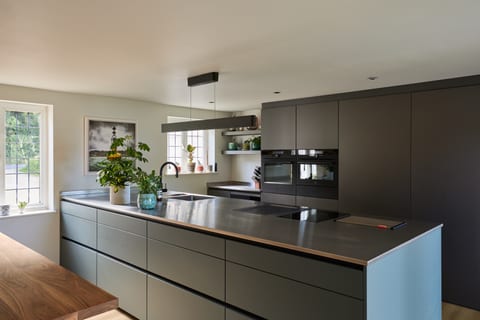 The Hever cabinetry wall with the concealed passage door closed; AEG ovens to the left, an open display niche to the right, the elevation reading as a single continuous plane.