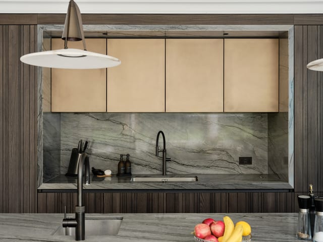 The Keston sink run framed within the dark timber elevation: light bronze wall units above, a Platino quartzite splashback and worktop, a matt black tap and an undermount sink.