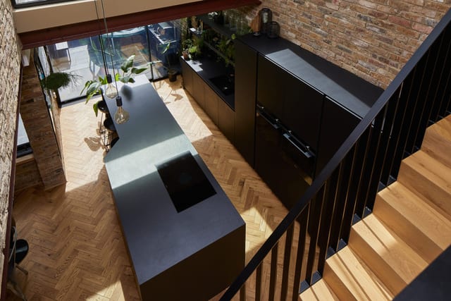 The Smith kitchen, Brockley — a matt-black island and tall cabinetry with integrated Gaggenau appliances, herringbone parquet and full-height glazing, seen from the staircase.