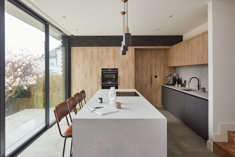 Matt anthracite base cabinetry with timber-effect tall units, a pale Caesarstone island and pendant lighting in a Beckenham kitchen.