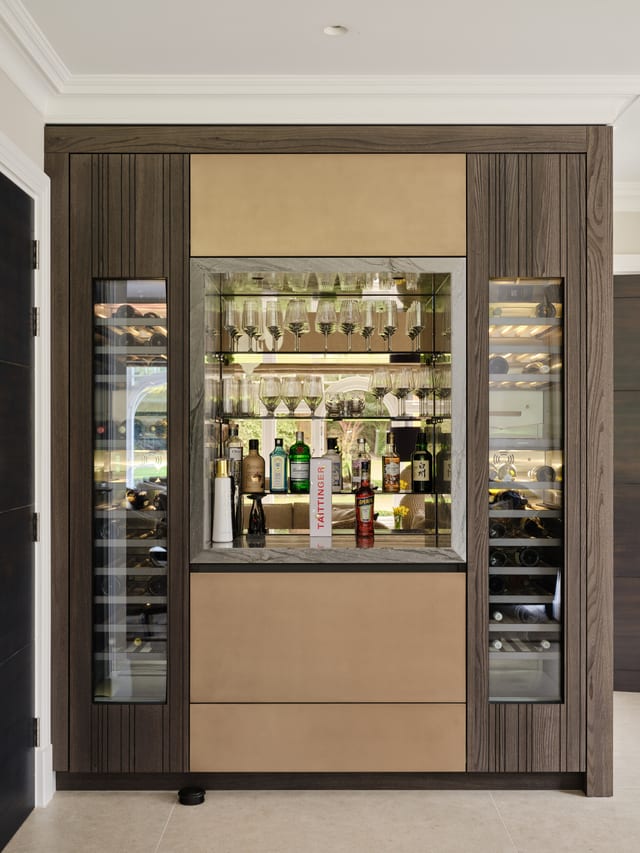 The Keston drinks area: a light bronze-lined niche with glassware and bottles, flanked by two glass-fronted wine cabinets, framed in Leicht Bahia dark timber.