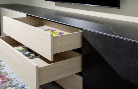 A close-up of a Sudbrock media unit: light-timber drawer boxes pulled open beneath a dark stone top, showing the drawer construction and finish.