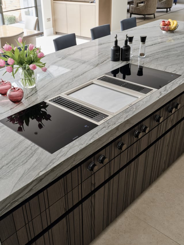 The Gaggenau 400 Series hobs set into the Platino quartzite island, with centre downdraft extraction, above dark timber drawers with bronze handles.