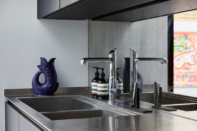 The antique-mirror splashback behind the stainless worktop run, reflecting the room, with the Quooker tap and integrated stainless sink.